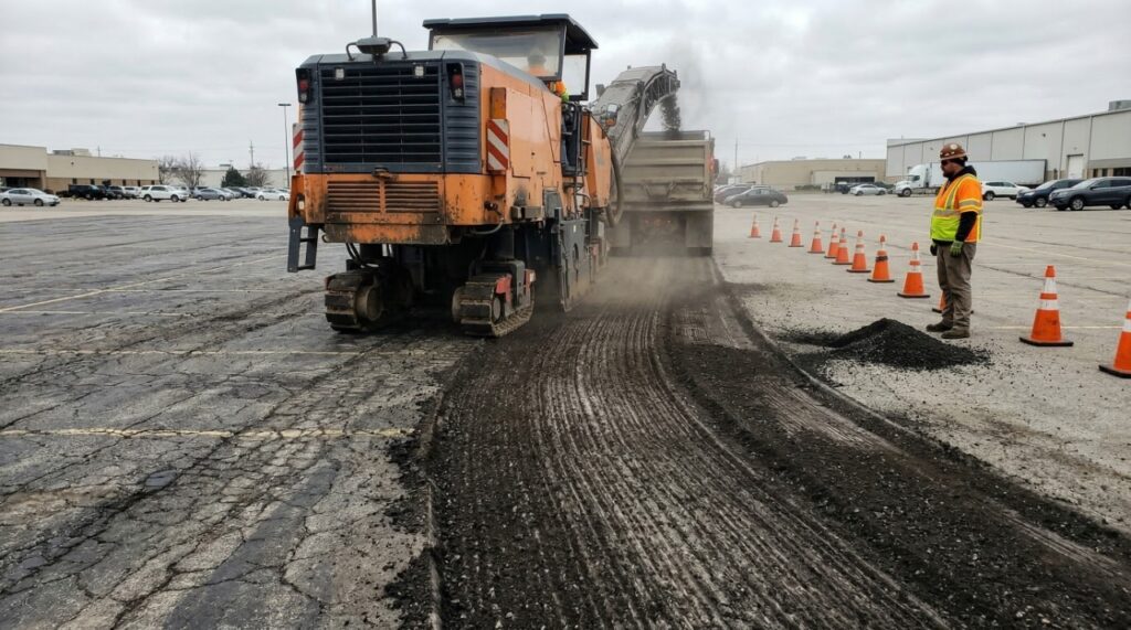 An authentic photo capturing a large commercial asphalt milling machine actively grinding a distressed parking lot surface in Indianapolis.