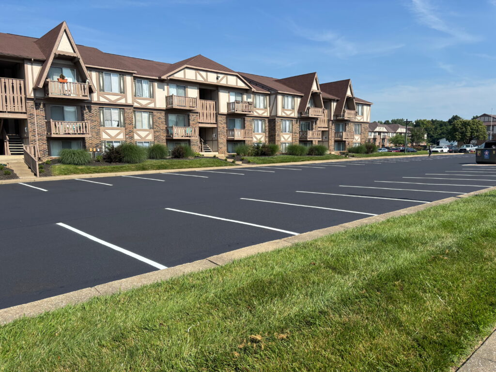 Freshly sealcoated and striped asphalt parking lot in front of a multi-story apartment complex.